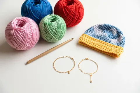 Yarn balls, a crochet hook, a crocheted hat and gold chain bracelets
